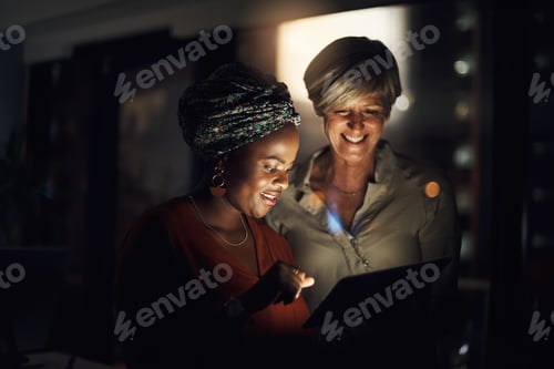 Preview: Shot of two businesswomen using a digital tablet together in an office at night