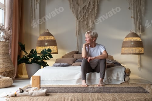 Preview: Portrait of senior woman on bed after yoga and looking at window