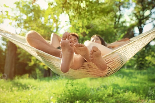 Preview: Young couple resting in comfortable hammock at green garden