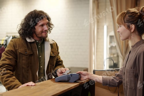 Preview: Young smiling male customer looking at pretty shop assistant