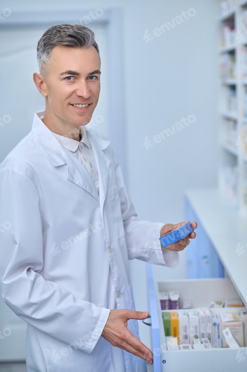Preview: Man in a lab coat standing near the shelves with medicines