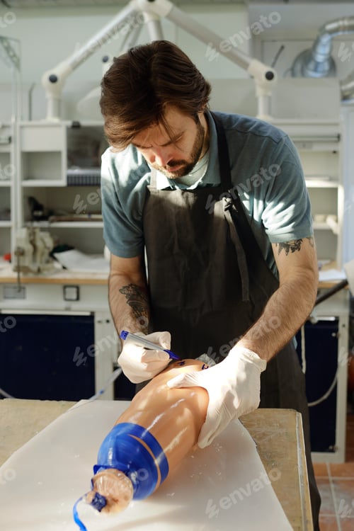 Preview: Male worker of prosthetic factory writing on silicone line with blue marker