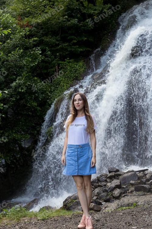 Preview: young girl in denim skirt and white t-shirt stopped by a waterfall