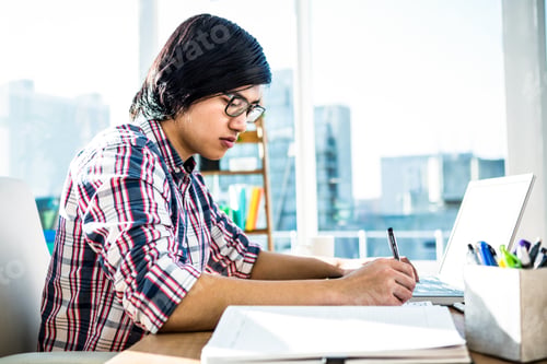 Preview: Hipster businessman writing while using laptop in office