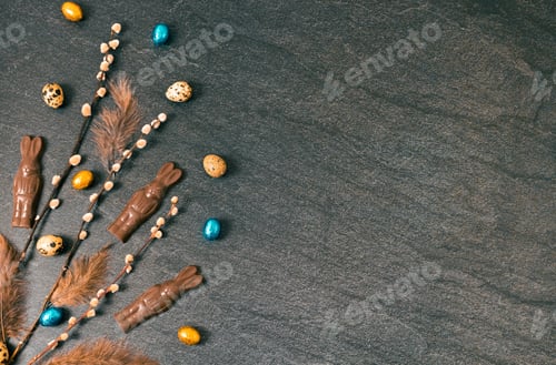 Preview: Chocolate bunnies, willow branches and Easter eggs on a black background.