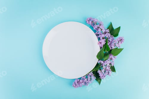 Preview: A plate with copy space around violet lilac on a blue background.