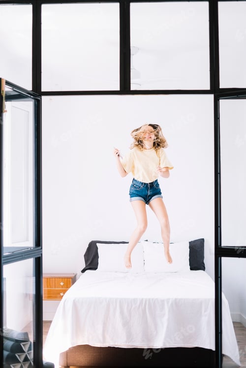 Preview: Excited woman with phone jumping on bed