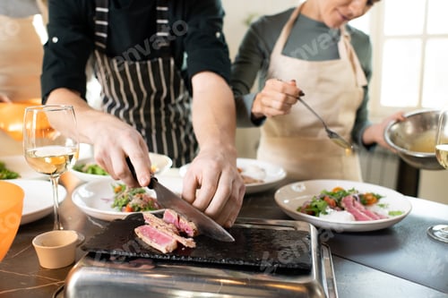 Preview: Hands of young male cooking coach chopping piece of smoked beef by table