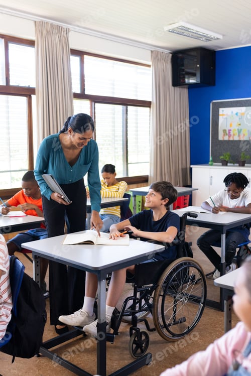 Preview: In school, Indian female teacher assisting student in wheelchair with classroom assignment