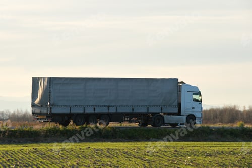 Preview: Semi-truck with cargo trailer driving on highway hauling goods in evening.