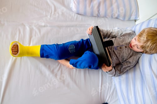 Preview: Little boy with broken leg playing on tablet