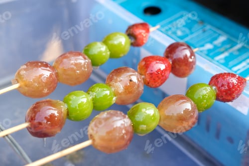 Preview: Close up of Tanghulu, Chinese street food candied fruit skewers with glossy grapes and strawberries.