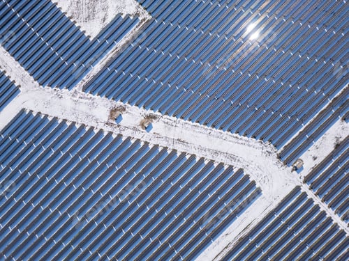 Preview: Aerial view of a large solar farm covered in snow, surrounded by a rural landscape with scattered