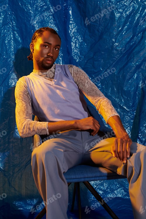 Preview: Handsome young man seated against a vibrant blue backdrop showcasing confident style