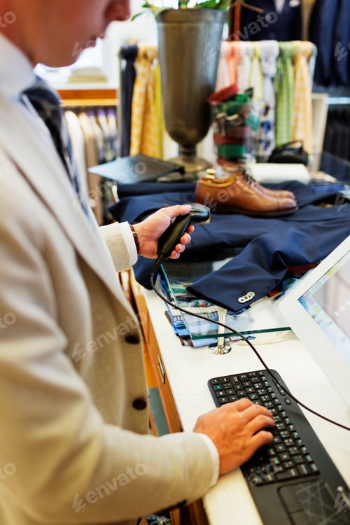Preview: Midsection of cashier holding bar code reader while using computer keyboard in showroom