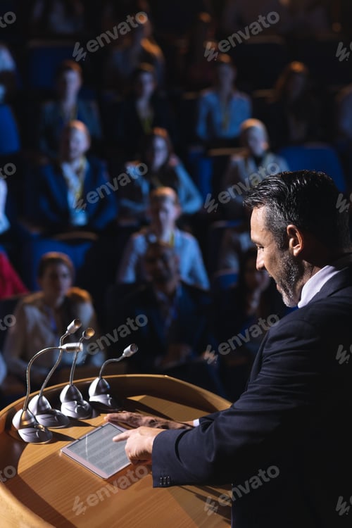 Preview: Businessman standing and looking at digital tablet on stage in auditorium