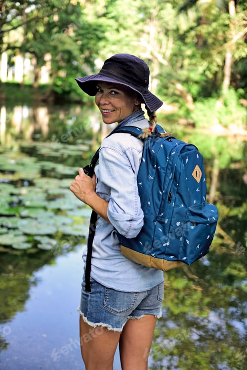 Preview: Portrait of smiling woman with backpack standing in front of a lake