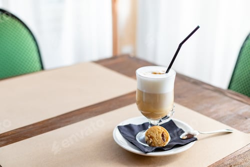 Preview: glass of Latte Macchiato with spoon, straw and plate with cookies on a wooden table.Delicious sweet