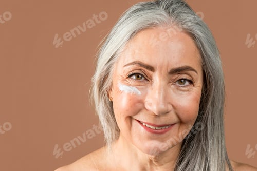 Preview: Happy old caucasian lady with natural beauty and cream on her face enjoy professional cosmetics