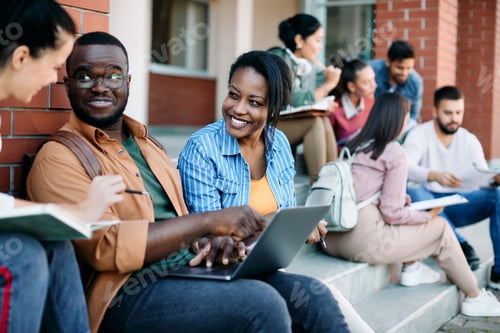 Preview: Group of happy university students talking and having fun while suing laptop at campus.
