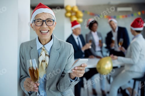 Preview: Happy mature businesswoman using mobile phone at New Year's party in the office.