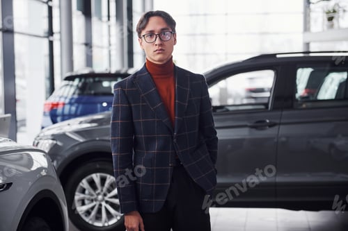 Preview: Posing for the camera. Young business man in luxury suit and formal clothes is indoors near the car