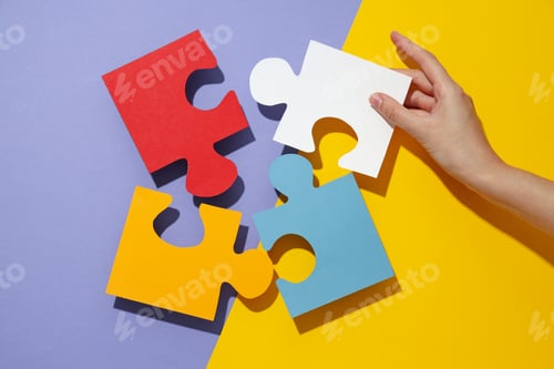 Preview: Colored paper puzzles and hand on yellow and purple background, top view