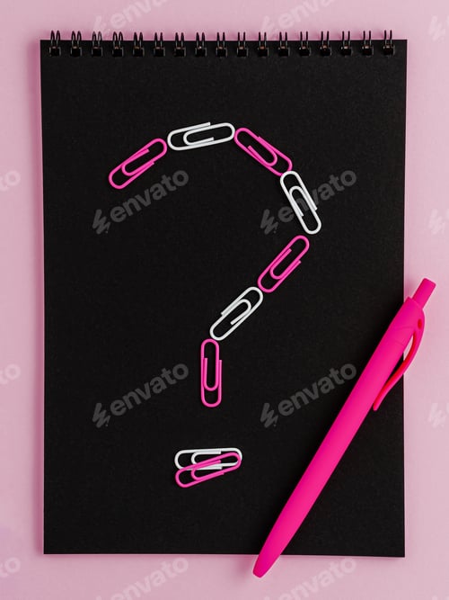 Preview: Question mark made of clips on black notebook blank on pink background. Flat lay.