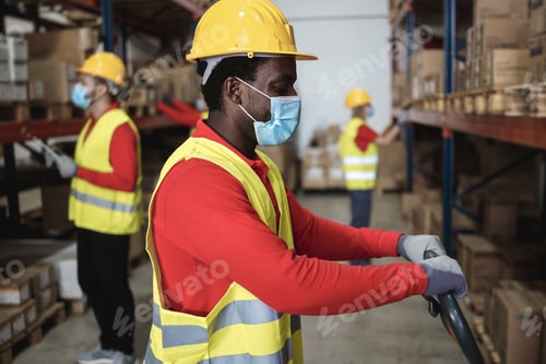 Preview: African warehouse worker loading delivery boxes while wearing safety mask - Focus on face