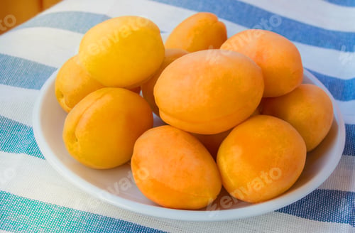 Preview: Fresh ripe apricots on a white plate on a striped tablecloth, on a Sunny summer day on the terrace