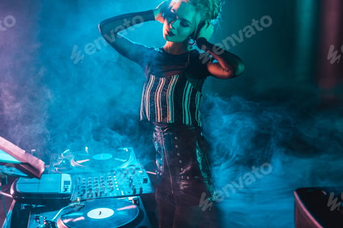 Preview: attractive dj woman with blonde hair listening music and touching headphones in nightclub with smoke