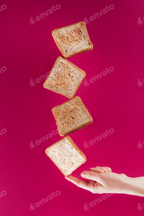 Preview: partial view of woman holding levitating toasts on finger isolated on pink