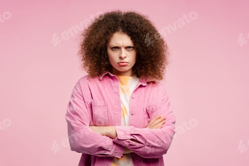 Preview: Sad, upset, young woman with curly hair, arms crossed looking at camera