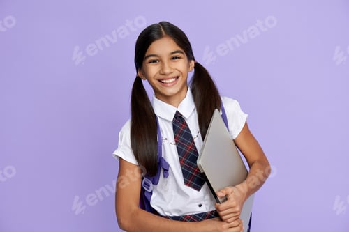 Vorschau: Glückliches indisches Schulmädchen in Uniform mit Laptop auf lila Hintergrund.