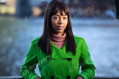 Preview: Pretty African American woman near a body of water wearing vibrant green jacket