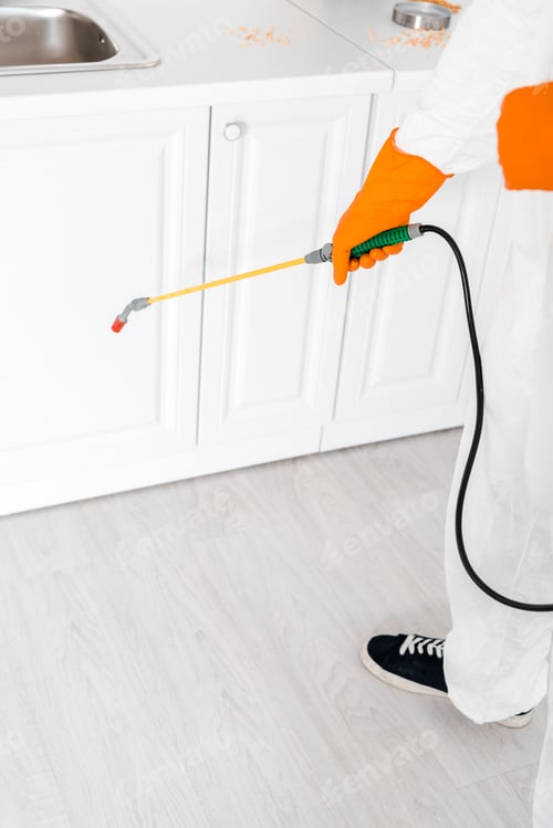 Preview: cropped view of exterminator in uniform standing with toxic spray near kitchen cabinet