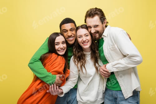 Preview: Cheerful multiethnic friends hugging isolated on yellow