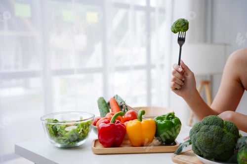 Preview: Woman holding broccoli with fork, preparing healthy meal with fresh vegetables