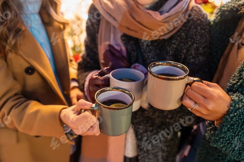Preview: Friends holding mugs of hot drinks at Christmas market, winter fashion, festive atmosphere