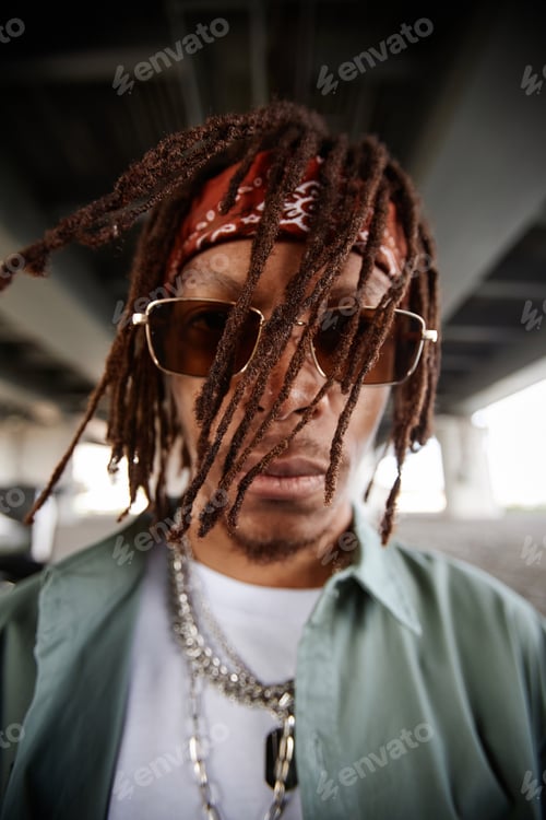 Preview: African American guy with dreadlocks looking at camera through sunglasses
