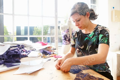 Preview: Designer intently crafting a new garment in her sunlit studio
