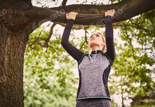 Preview: Young woman doing pull ups on park tree branch