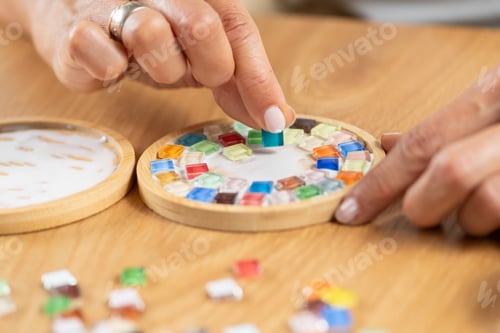 Preview: Female hands assembling coasters by gluing small decorative parts