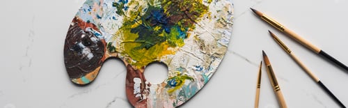 Preview: top view of colorful palette with oil paints near paintbrushes on marble white surface, panoramic
