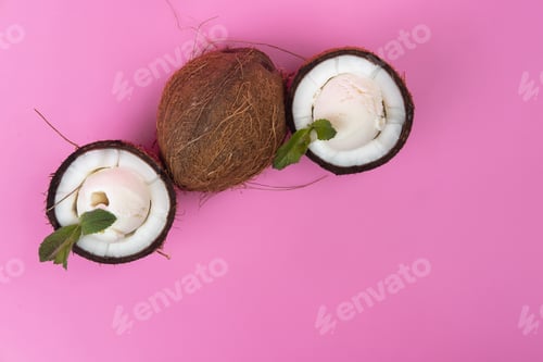 Preview: Vanilla ice cream balls in fresh coconut halves decorated with mint leaves on a pink background