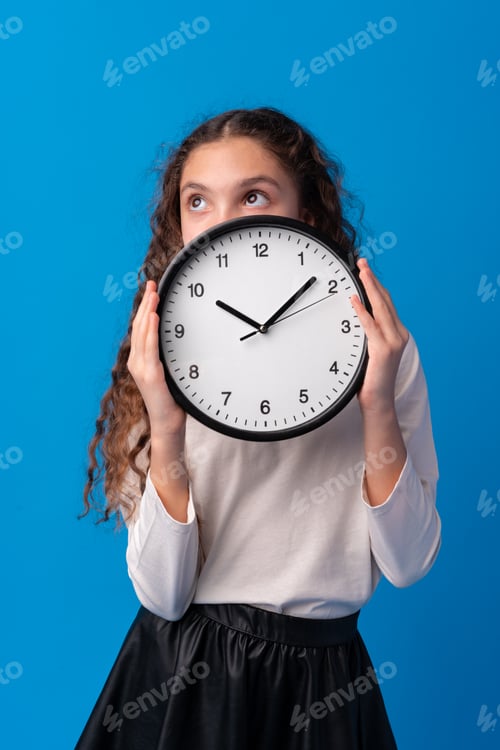 Preview: Beautiful teen girl holding wall clock over blue background