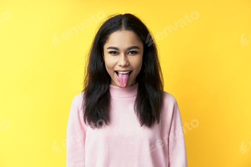 Preview: Pretty black woman showing tongue and looking at the camera on yellow background