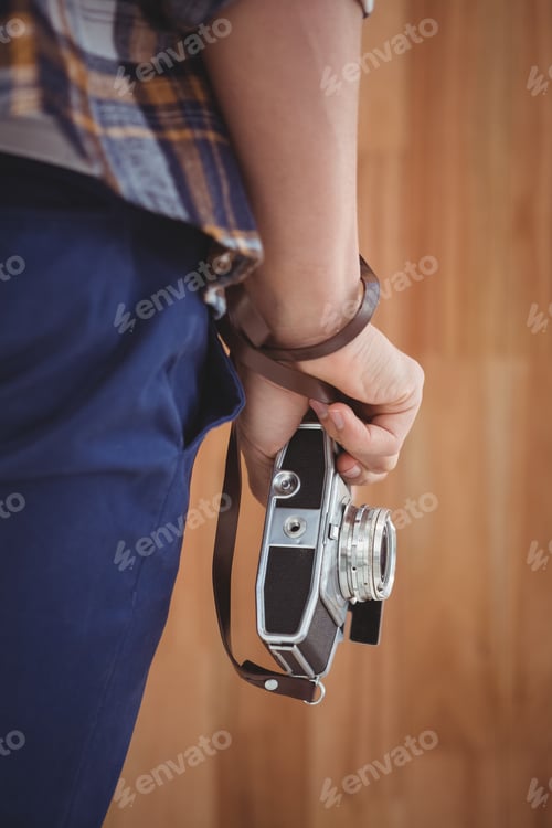 Preview: Cropped image of man holding camera against wooden wall in office