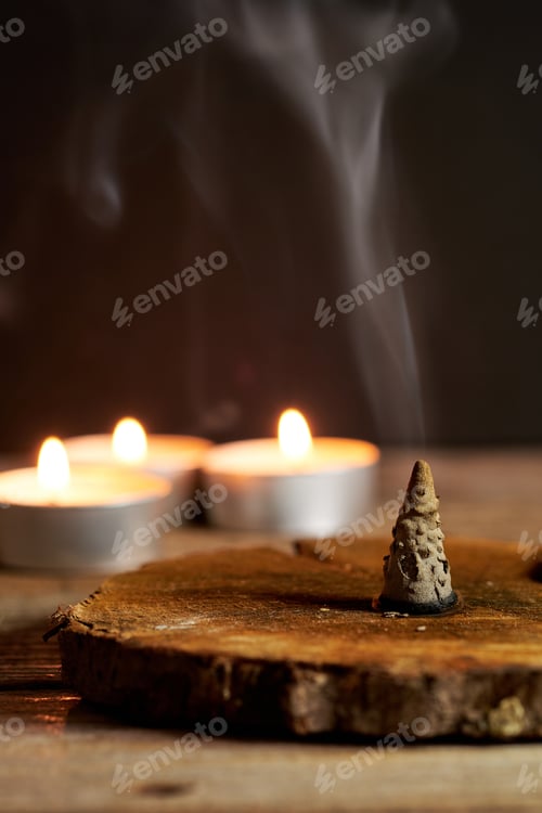 Preview: Incense Cone Burning on Wooden Base With Candles Glowing Softly