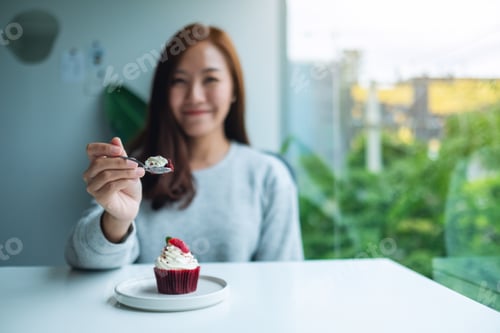 Preview: A beautiful asian woman holding and eating red velvet cup cake